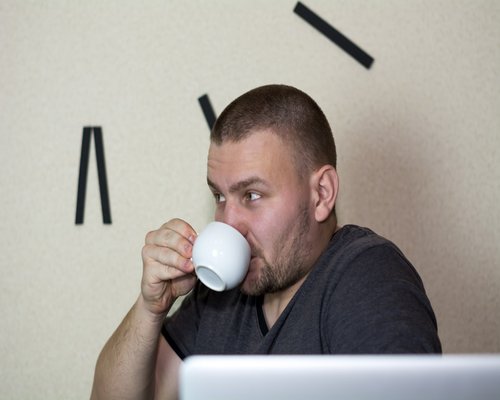 A person looking at a clock while drinking a cup of coffee